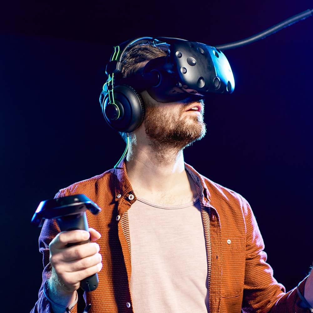 Man playing game using virtual reality headset and gamepads in the dark room of the playing club