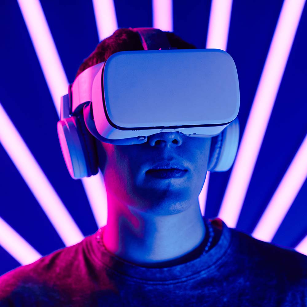 Futuristic shot of young man wearing VR headset with neon light beams in background, copy space